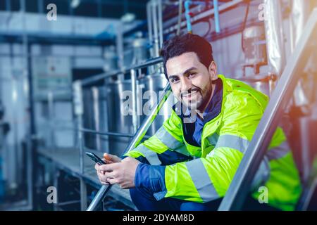 Portrait sourire heureux intelligent latino travailleur assis détendez-vous dans l'industrie de l'usine main tenant smartphone bleu effet colortone. Banque D'Images