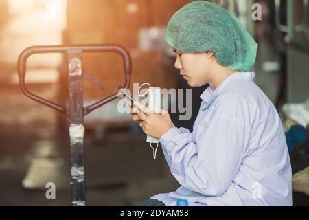 Une jeune femme birmane asiatique travaille pour se détendre, jouant au téléphone portable, attendant des quarts de travail dans une usine d'hygiène alimentaire. Banque D'Images