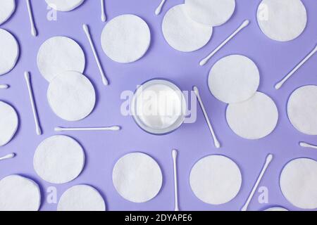 Crème hydratante en pot en verre ouvert, tampons de coton et bâtonnets de coton sur fond violet clair texturé. Vue de dessus. Bio bio naturel bio bio éco soin de la peau bea Banque D'Images