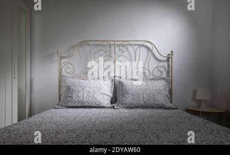 Vue de face d'une chambre intérieure de style classique avec lit double, tête de lit forgée, linge de lit en dentelle sur fond de mur blanc Banque D'Images