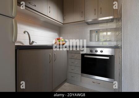 Intérieur moderne d'une petite cuisine d'angle avec carreaux de briques de métro blancs éclabous. Assiette de fruits sur fond d'armoires en bois clair Banque D'Images