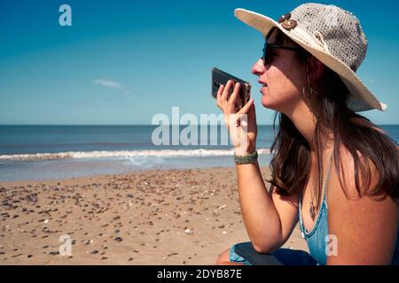 Une femme sur la plage envoyant un message vocal, paysage marin en arrière-plan Banque D'Images