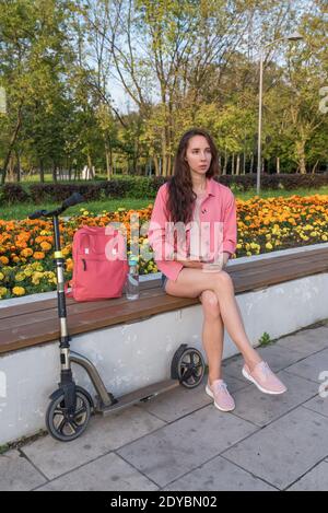 Femme en ville en été assis sur le banc, écoute de messagerie vocale en ligne chat application réseaux sociaux Internet, tenant le smartphone, repos après le travail Banque D'Images