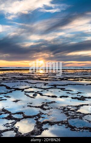 Une vue verticale d'un beau coucher de soleil sur l'océan avec plage rocheuse et piscines à marée en premier plan Banque D'Images