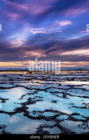 Une vue verticale d'un beau coucher de soleil sur l'océan avec plage rocheuse et piscines à marée en premier plan Banque D'Images