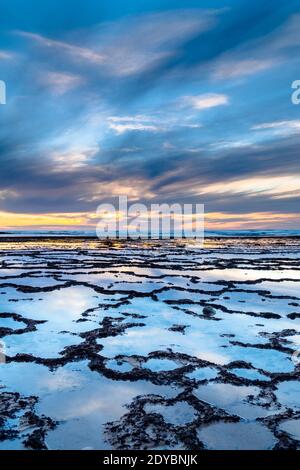 Une vue verticale d'un beau coucher de soleil sur l'océan avec plage rocheuse et piscines à marée en premier plan Banque D'Images