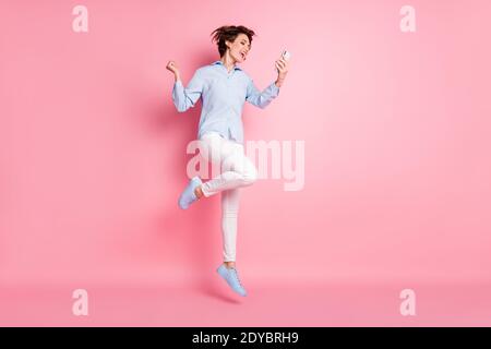 Pleine photo de profil de jolie dame bonne humeur saut haut en haut de l'air étudiant de navigation téléphone de chat amis célébrer le week-end portez un pantalon-chemise bleu Banque D'Images