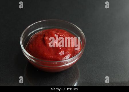 pâte de sauce tomate rouge dans un bol de sauce en verre sur fond noir copier l'espace pour le texte. Banque D'Images