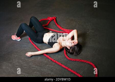 Femme fatiguée en vêtements de sport couchés sur le sol après une tenue intensive musculation à la salle de gym Banque D'Images