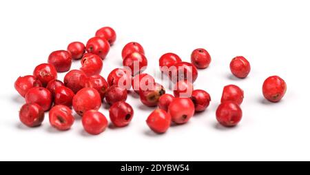 Grains de poivre rouge ou rose éparpillés à bord, photo de gros plan isolée avec fond blanc Banque D'Images