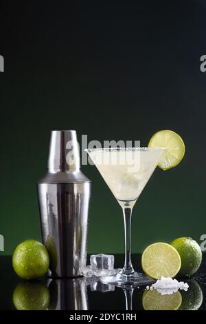 Cocktail mexicain typique de margarita avec tranche de citron vert et shaker à cocktail sur fond noir et vert. Banque D'Images