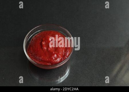 pâte de sauce tomate rouge dans un bol de sauce en verre sur fond noir copier l'espace pour le texte. Banque D'Images