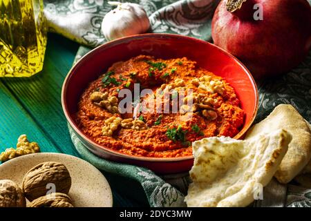 Plat moyen-oriental. Tartiner de poivron rouge rôti - muhammara - dans un bol rouge sur fond de bois bleu-vert avec divers ingrédients Banque D'Images