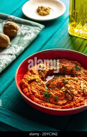 Plat moyen-oriental. Tartiner de poivron rouge rôti - muhammara - dans un bol rouge sur fond de bois bleu-vert avec divers ingrédients Banque D'Images