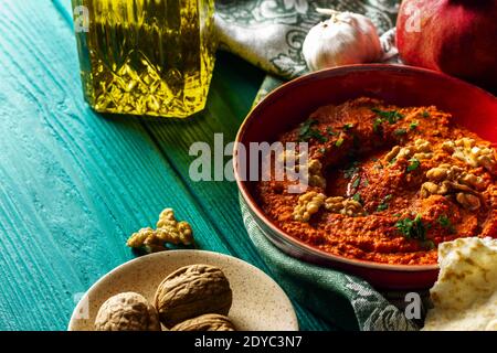 Plat moyen-oriental. Tartiner de poivron rouge rôti - muhammara - dans un bol rouge sur fond de bois bleu-vert avec divers ingrédients Banque D'Images