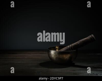 Ancien bol de chant tibétain sur fond en bois, fond noir. Musicothérapie. Banque D'Images