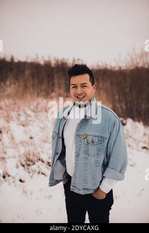 Homme hispanique brunette avec barbe en veste denim en hiver au milieu de la neige. Mode de rue pour hommes style décontracté 2021 Banque D'Images