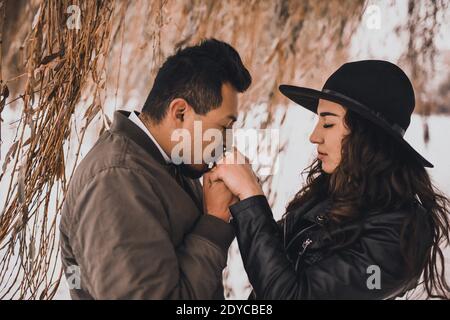 L'homme mexicain tient les mains d'une femme ukrainienne dans une veste en cuir noir et un chapeau noir sur la nature en hiver. Amour entre les différentes nationalités Ven Banque D'Images