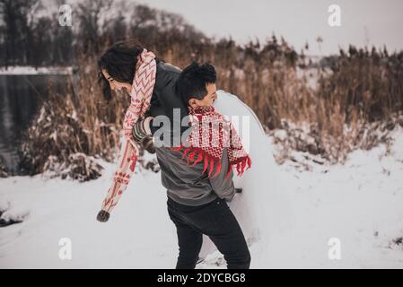 un jeune homme et une jeune femme qui coure dans la neige en riant se moquant d'avoir du plaisir à jouer snowballs.bride et de la groom dans l'amour couple en écharpe tricotée et Banque D'Images