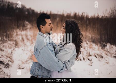 Mexicain hispanique homme en denim veste surdimensionnée et femme embrasse embrassant rire. Marié et mariée mariage amour couple en hiver dans la neige. Fashiona Banque D'Images
