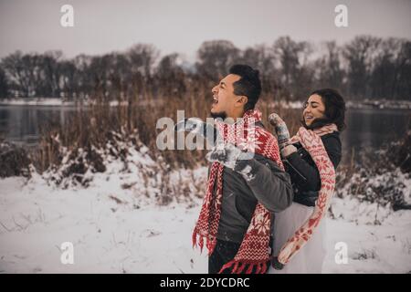 couple de mariage couchant dans la neige riant s'amuser à jouer boules de neige Banque D'Images