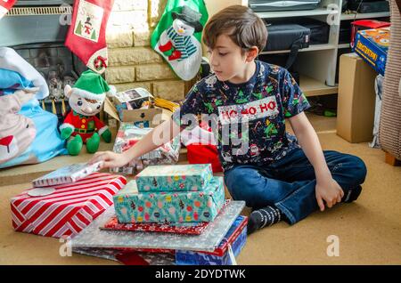 Un garçon est assis à pieds croisés sur le sol avec une pile de cadeaux de Noël qu'il est sur le point d'ouvrir. Banque D'Images