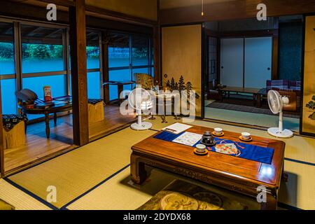 Une pièce tatami traditionnelle avec des portes coulissantes en papier translucide s'ouvre sur une rivière brumeuse près de Kakegawa, au Japon, une table laquée noire garnie de bols à thé au premier plan. Banque D'Images