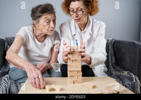 Jeu Jenga. Le thème est la démence, le vieillissement et les jeux pour les personnes âgées. La femme âgée caucasienne construit une tour de blocs de bois avec l'aide d'un médecin en tant que partie Banque D'Images