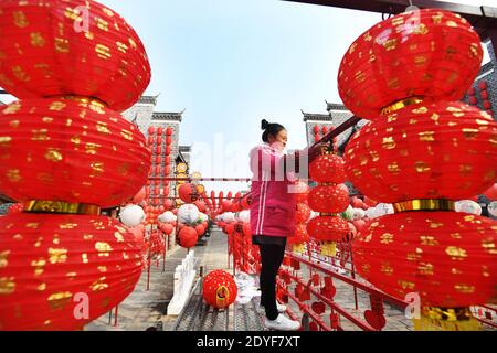 Beijing, province chinoise du Jiangxi. 25 décembre 2020. Un membre du personnel est suspendu à des lanternes rouges dans un bloc historique et culturel de la ville de Zhangshu, dans la province de Jiangxi, dans l'est de la Chine, le 25 décembre 2020. À l'approche du jour de l'an, des décorations de fête sont vues dans les rues et les ruelles de la ville. Credit: Zhou Liang/Xinhua/Alay Live News Banque D'Images