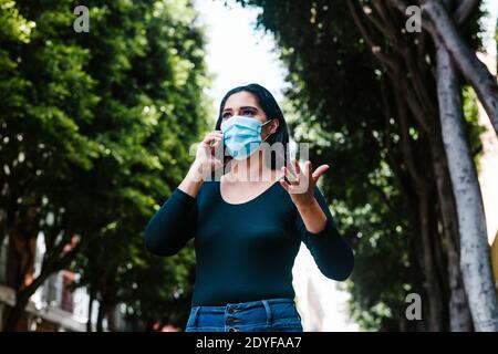 Une femme mexicaine avec un masque de visage appelant par téléphone pendant qu'elle est Marche dans la rue d'une ville d'Amérique latine Banque D'Images
