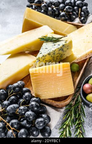 Assiette de fromages servie avec des raisins, des craquelins, des olives et des noix. Assortiment de délicieux en-cas. Arrière-plan gris. Vue de dessus Banque D'Images