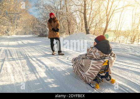 Une mère avec un enfant marche un matin d'hiver glacial le jour du soleil. Bébé enveloppé dans une couverture sur un traîneau Banque D'Images