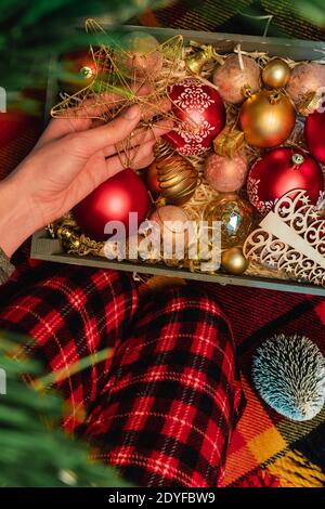 Vacances d'hiver. Noël traditionnel décorant l'arbre de Noël dans le style rustique. Jeune femme en pantalon à carreaux sur tissu écossais avec boîte en bois de rouge et d'or Banque D'Images