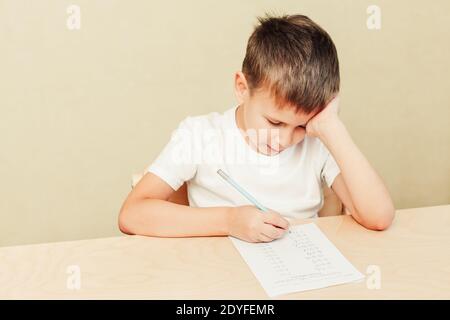 enfant de 7 ans, garçon assis au bureau et écrivant en feuille de papier Banque D'Images