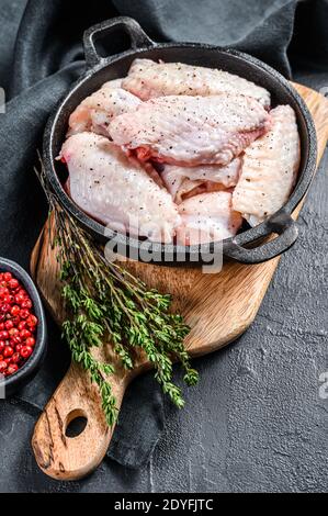 Ailes de poulet crues avec épices et herbes dans une casserole. Arrière-plan noir. Vue de dessus Banque D'Images