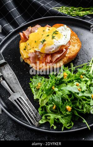 Hamburger petit déjeuner avec bacon, œuf Benedict, sauce hollandaise sur brioche. Arrière-plan noir. Vue de dessus Banque D'Images