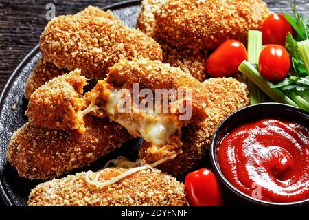 Suppli al telefono italian fast food - croquettes de riz frites farcies à la mozzarella servies sur une assiette noire avec des branches de céleri, des tomates et du ketchup Banque D'Images