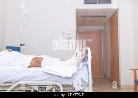 Patient allongé dans le lit d'hôpital avec une jambe cassée. Concept d'hospitalisation et de soins médicaux. Banque D'Images