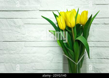 Bouquet de tulipes jaunes dans un vase en verre sur un arrière-plan en pierre blanche Banque D'Images