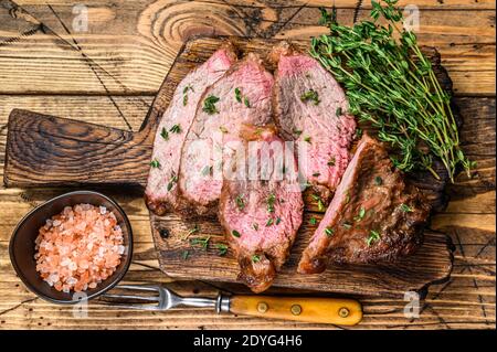 Tranches rares de rôti de boeuf sirloin à trois pointes steak bbq sur une planche à découper en bois. fond en bois. Vue de dessus Banque D'Images