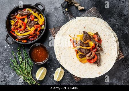 Bœuf Steak Fajitas à la tortilla, mélanger le poivre et l'oignon cuisine mexicaine traditionnelle. Arrière-plan noir. Vue de dessus Banque D'Images