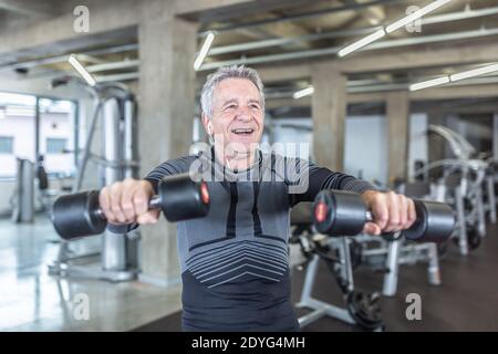Dans ses années 60, un homme fait de l'exercice en haltère dans le centre de remise en forme. Banque D'Images