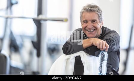 En taille dans ses années soixante, l'homme repose sur une serviette souriante à l'intérieur de la salle de gym. Banque D'Images