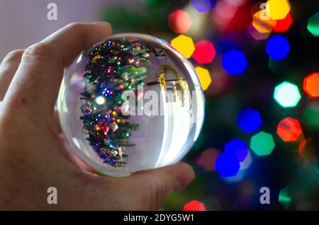 Regarder un arbre de Noël avec des lumières colorées à travers une boule de lentille. L'arbre de Noël lui-même est considéré comme un bokeh coloré en arrière-plan. Banque D'Images