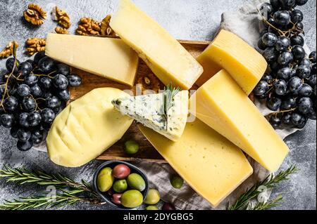 Différents morceaux de fromage avec des olives de noix et des raisins. Assortiment de délicieux en-cas. Arrière-plan gris. Vue de dessus Banque D'Images