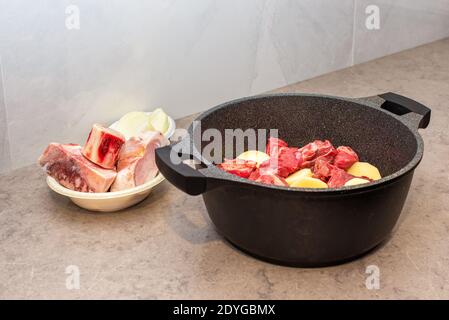 Gros plan du Hamin traditionnel juif Cholent - plat principal pour le repas de Shabbat bœuf lentement cuit avec pommes de terre, haricots, grains de blé, marrowbone, et épices dans une casserole sur une table de cuisine en marbre gris. Banque D'Images