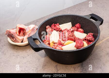 Gros plan sur le Hamin traditionnel juif Cholent - plat principal pour le repas de Shabbat bœuf lentement cuit avec des pommes de terre, des haricots, des grains de blé et des épices dans une casserole sur une table de cuisine en marbre gris. Banque D'Images