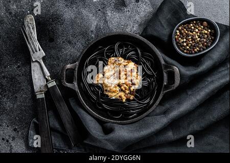 Pâtes à spaghetti noires avec de l'encre calmar dans une casserole. Bœuf sauce au poivre. Arrière-plan noir. Vue de dessus Banque D'Images