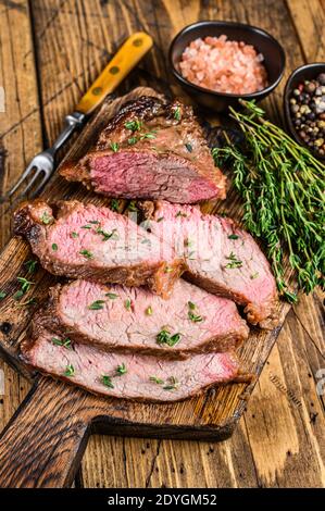 Tranches rares de rôti de boeuf sirloin à trois pointes steak bbq sur une planche à découper en bois. fond en bois. Vue de dessus Banque D'Images