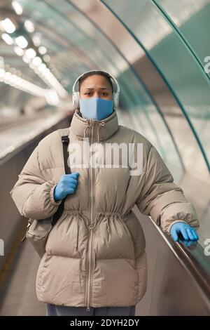 Portrait d'une jeune femme en veste chaude et protectrice masque et gants regardant la caméra en se tenant sur l'escalier roulant Banque D'Images